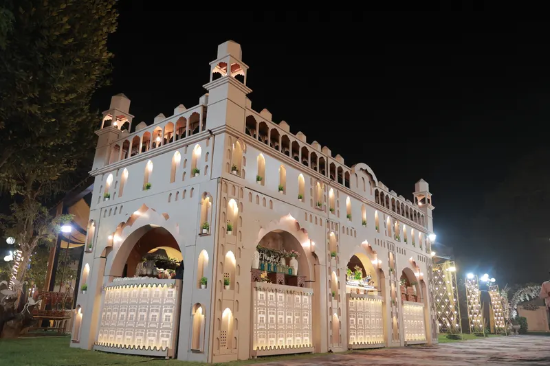Illuminated Nawabi-arch façade housing mocktail and live food counters at a night event